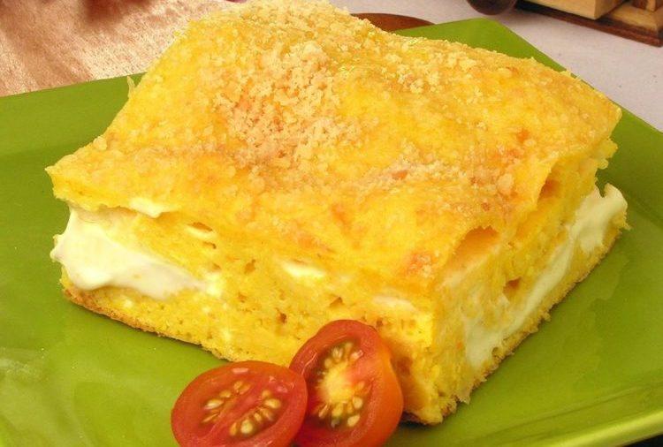 Pedaço da Torta de milho cremosa. A torta está servida em um prato verde, o recheio está derretendo. Um tomate-cereja fatiado ao meio está decorando o prato.