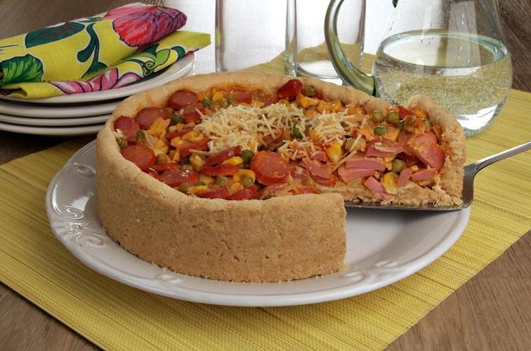 receita de torta aberta de cachorro-quente, feita em uma fôrma redonda, com salsicha, queijo, ervilha e milho.