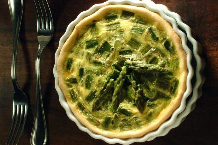 A fotografia da Torta de aspargo foi tirada de cima para baixo. Dessa forma vemos toda a superfície da torta. O recheio é de aspargos gratinados, juntamente com o queijo parmesão derretido. Ao lado da torta estão dois garfos.