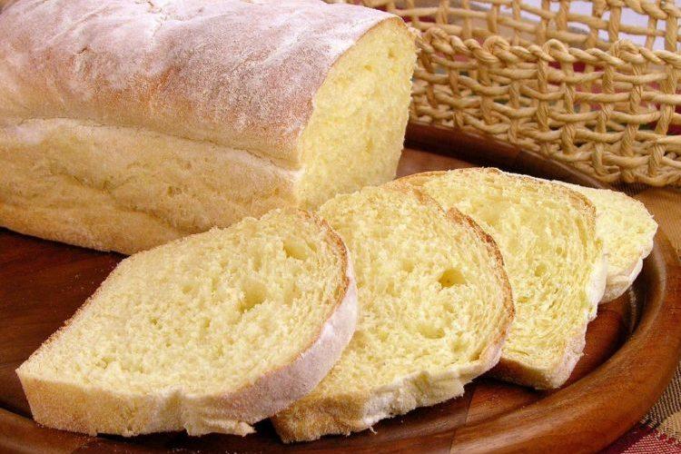 Pão de mandioquinha polvilhado com farinha e fatiado sobre uma tábua de madeira. 