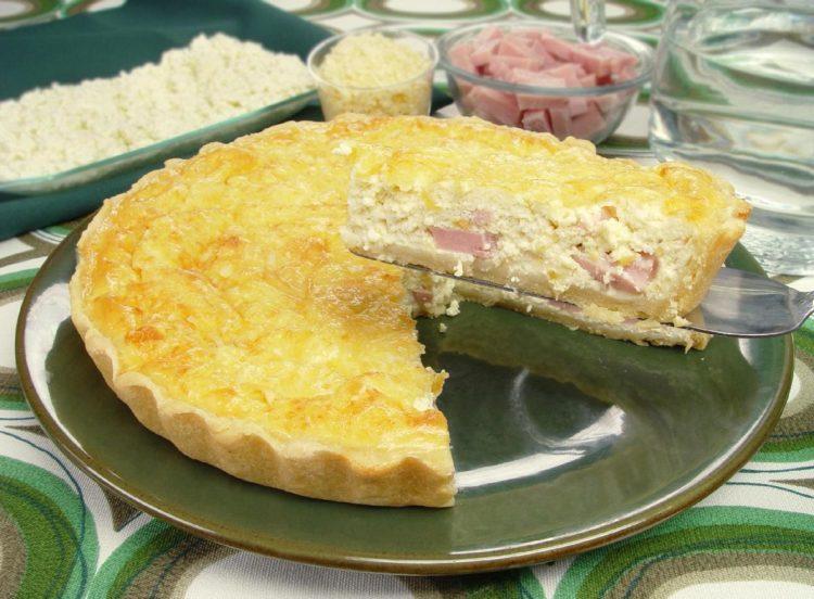 Foto com a receita da Quiche de presunto e queijo. A receita está em uma travessa de vidro, e a foto está focada em um pedaço da quiche, recheada com queijo e presunto