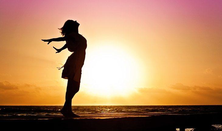 Matrimônio. Na foto, mulher com os braços abertos e o por do sol no fundo