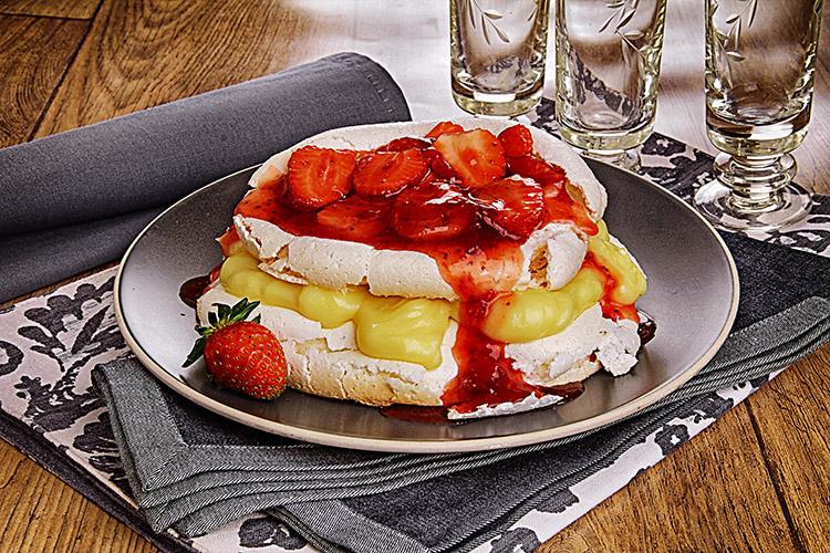 Pavlova de morango no prato com calda e morangos por cima.