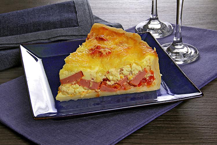 Pedaço de quiche de salsicha em um prato quadrado azul com duas taças ao lado.