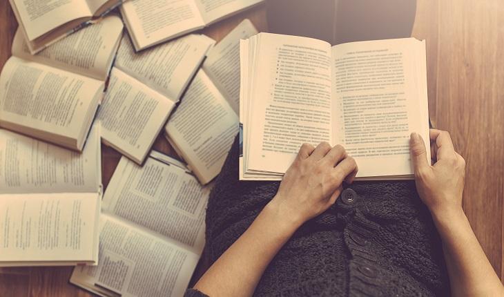 A foto mostra uma mulher em sua rotina de estudos com um monte de livros abertos