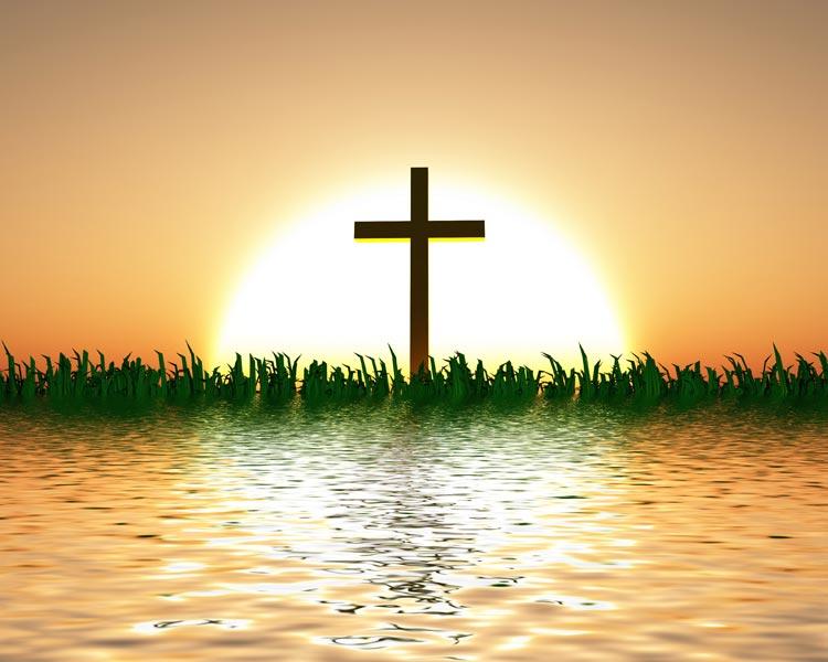 Cruz com sol ao fundo, gramas e lago