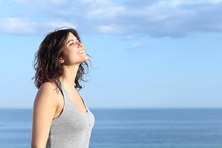 Mulher com cabelo de verão tomando sol na praia, na frente do mar