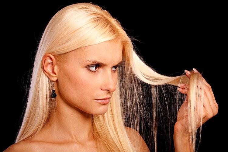 Mulher loira olhando uma mecha do cabelo de verão