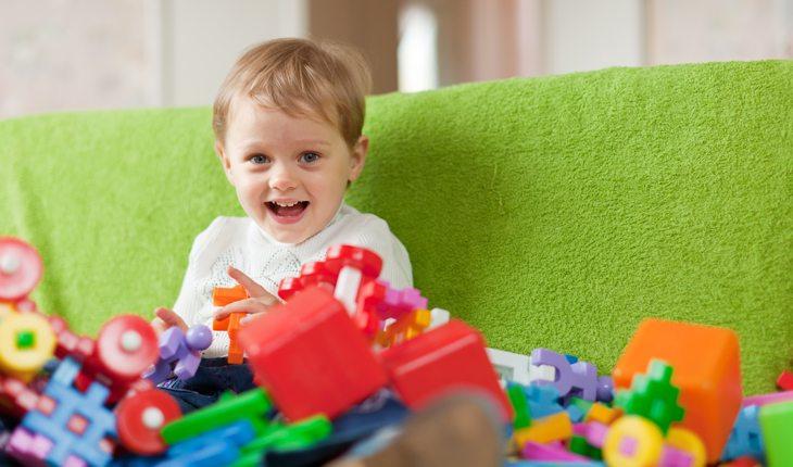 criança brincando com vários legos, sentada em um sofá verde