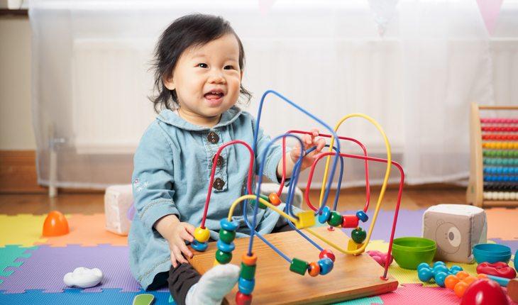 criança sentada num tapete colorido com vários brinquedos