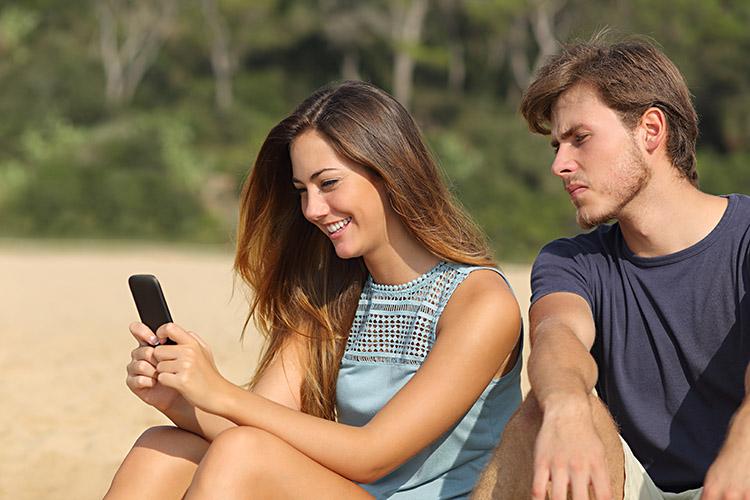 mulher mexendo no celular enquanto o homem está sentado ao lado dela olhando