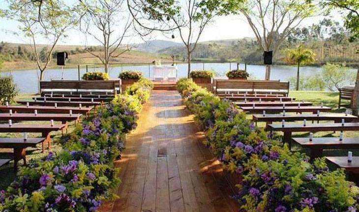 Foto de cerimônia de casamento em bancos e chão de madeira ao ar livre.