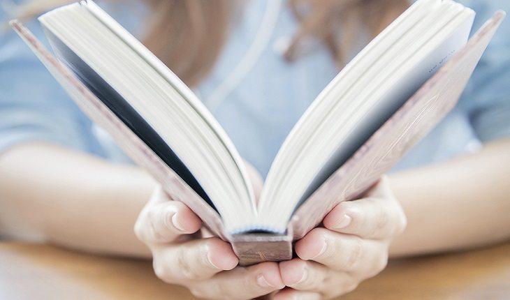 A foto mostra uma mulher segurando um livro aberto com as duas mãos, ilustrando uma das leis morais do espiritismo