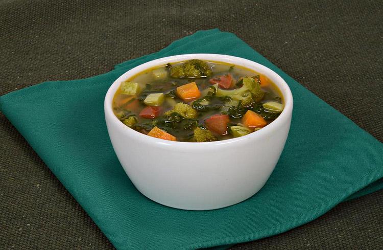 Sopa detox com legumes de coloração verde com dentro de uma travessa branca pequena