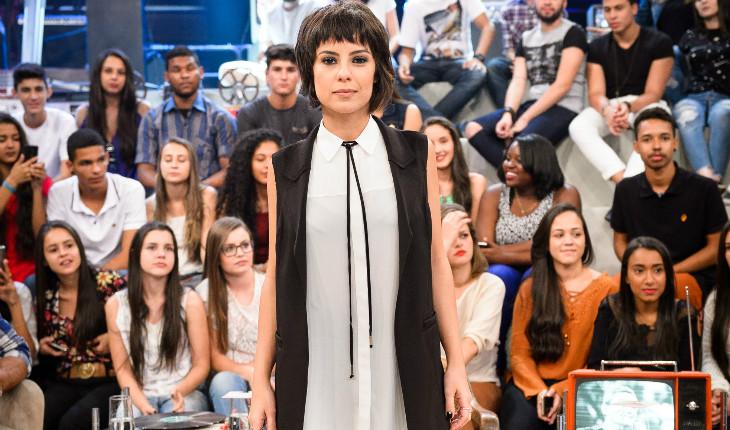 Andreia Horta, em pé, usando vestido cinza e colete preto