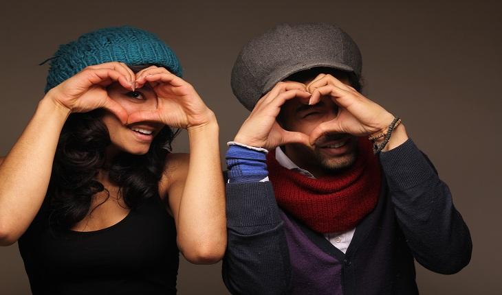 Casal com roupas de inverno fazendo um coração com as mãos