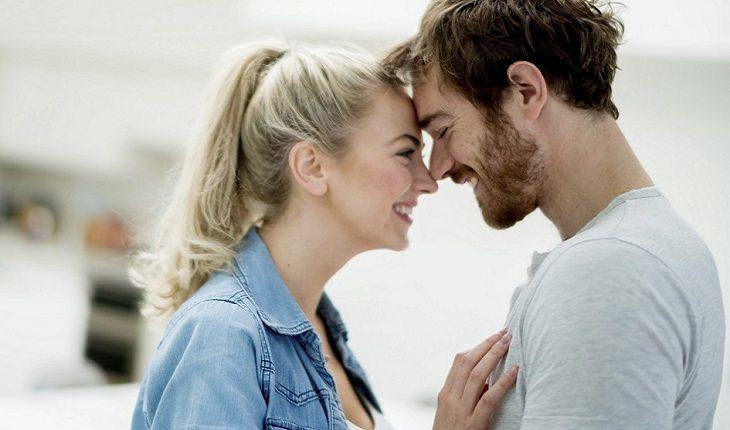 A foto mostra um casal sorrindo com as cabeças encostadas