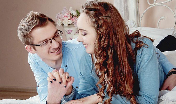 Casal de mãos dadas sorrindo deitado em uma cama