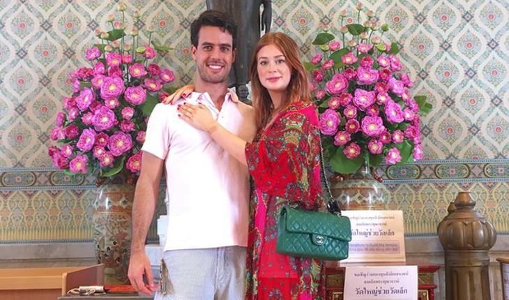 Marina abraça o marido posando para foto em frente à dois vasos com flores cor de rosa