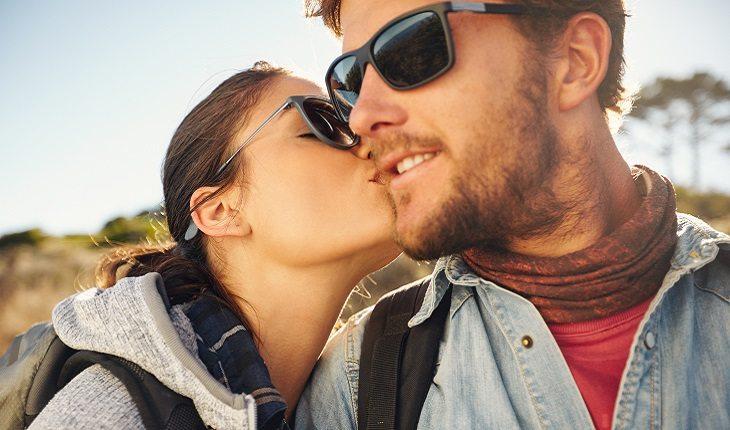 A foto mostra uma moça beijando o namorado no rosto