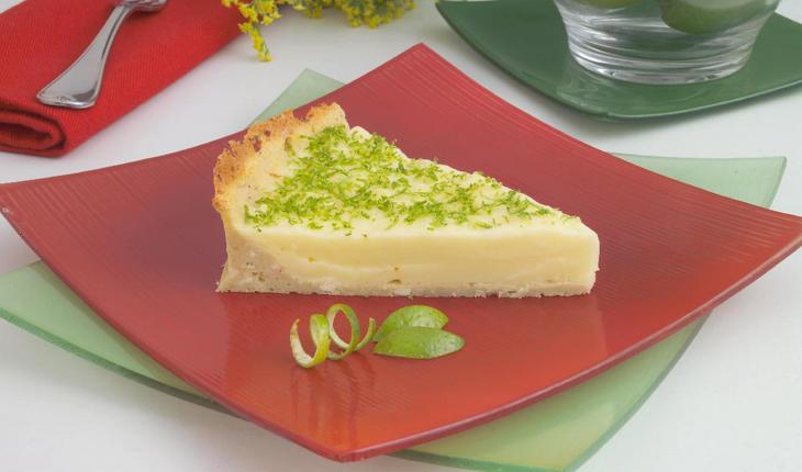 Imagem de uma torta light de limão sobre um prato vermelho, com rodelas de limão enfeitando.