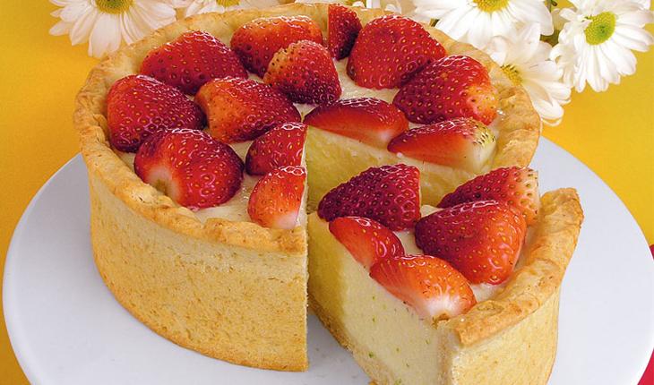 Imagem de torta light de morango sobre um prato branco. Para enfeitar algumas margaridas. Uma fatia já está cortada.