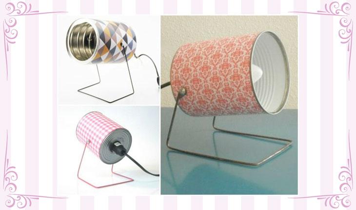 Na imagem há uma foto de uma luminária feita com latas decoradas. Ao redor há uma moldura branca com detalhes em rosa.