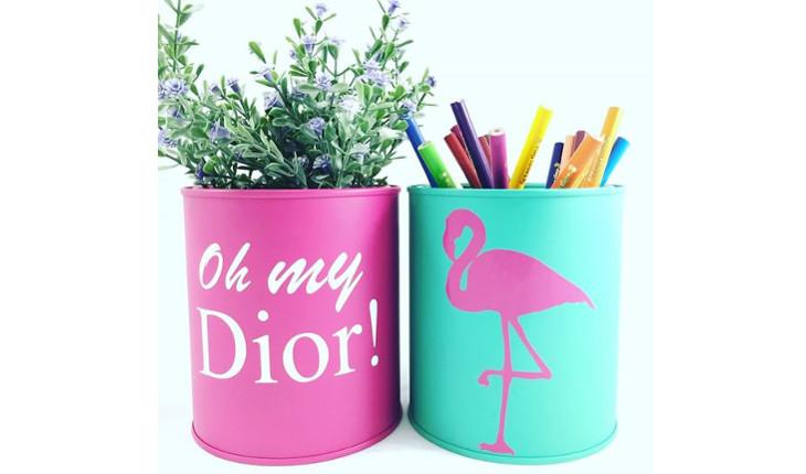 Na foto há duas latas de aço revestidas com adesivos coloridos, sendo a primeira em rosa e a segunda em azul. Na primeira há os escritos 