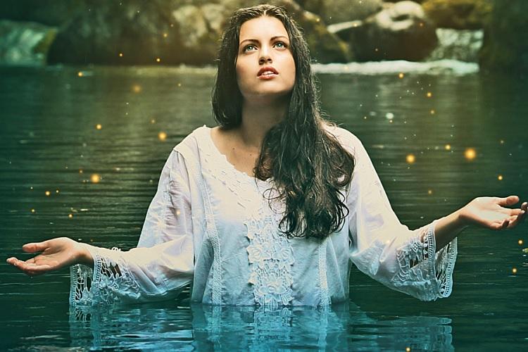 A foto mostra uma mulher espírita em um lago olhando para cima com os braços abertos. Tipos de obsessões