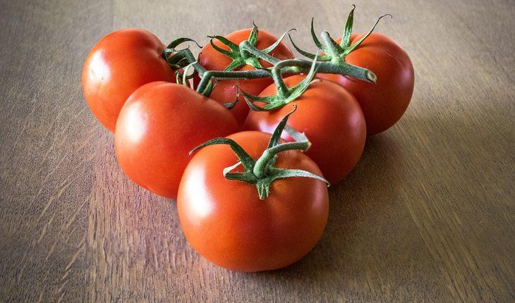 Imagens de cincos tomates vermelhos em cima de uma superfície de madeira