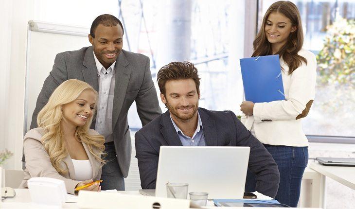 foto de uma equipe de trabalho em volta de um computador, como um homem, como se fosse o chefe, apontando para a tela