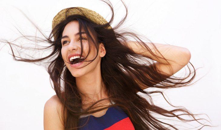 Mulher de cabelo castanho espalhado pelo vento e segurando chapéu