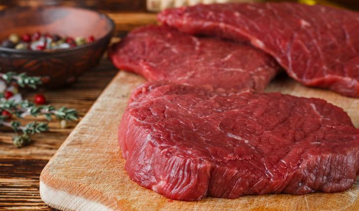 Bifes de carne crua vermelha em cima de tábua de madeira