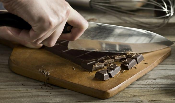 Faca cortando barra de chocolate em cima de tábua de madeira