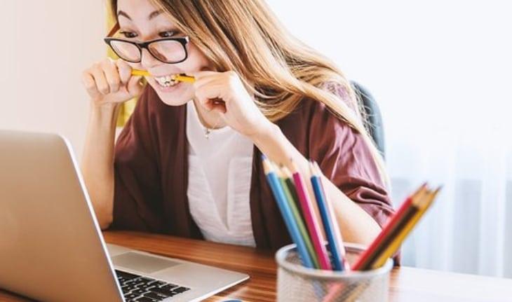 mulher asiática de óculos mordendo lápis e usando notebook