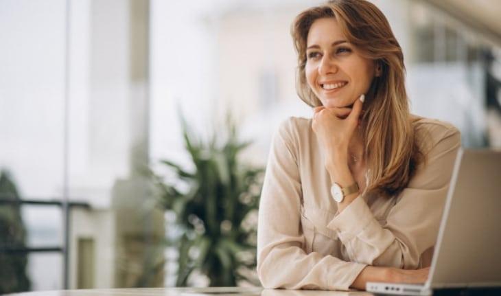 mulher branca sentada sorrindo apoiando a cabeça na mão